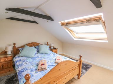 A bedroom with a wooden bed with blue patterned bedding two bedside tables with lamps and a skylight window at Taliharris Cottage in Llandysul