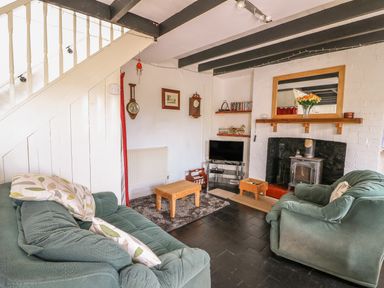 A living room with green sofas a wooden coffee table a fireplace with a mirror above and a tv under wooden stairs at Taliharris Cottage in Llandysul
