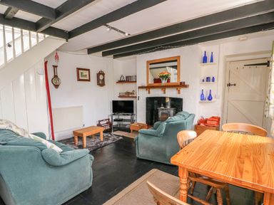 A living room with green sofas a wooden dining table and chairs a TV and a wood burning stove at Taliharris Cottage in Llandysul