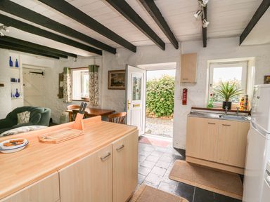 A kitchen and dining area with wooden cabinets and a table next to an open door at Taliharris Cottage in Llandysul