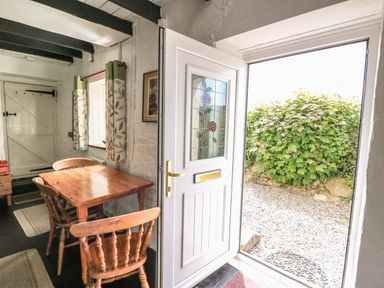 A dining area with a wooden table and chairs next to an open door showing a garden outside at Taliharris Cottage in Llandysul