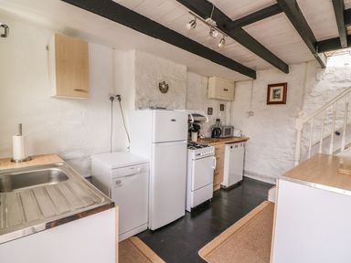 A kitchen with a sink dishwasher refrigerator stove microwave and stairs at Taliharris Cottage in Llandysul