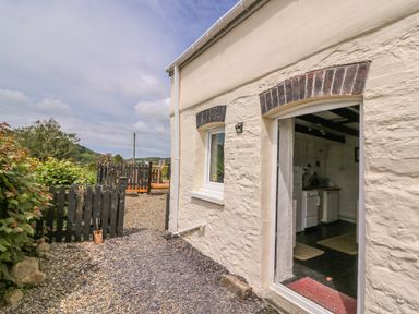 Exterior view of a cottage with a doorway to a kitchen and a small fenced garden area with chairs at Taliharris Cottage in Llandysul