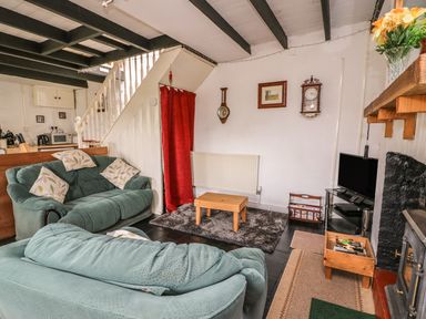 A living room with two sofas a small wooden coffee table a television and a staircase with a red curtain at Taliharris Cottage in Llandysul