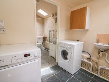 A laundry room with washing machine dryer small sink and cabinet next to a bathroom at Taliharris Cottage in Llandysul
