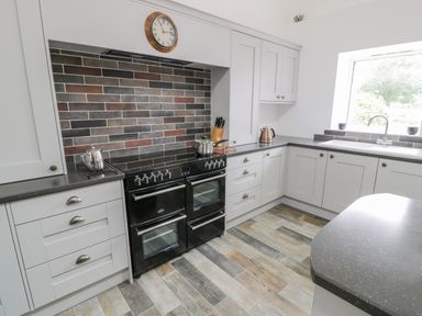 A kitchen with a black double oven, gray cabinets, a tiled backsplash, and a window at Sgubor in Pentraeth