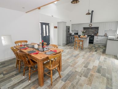 A kitchen and dining area with a wooden dining table set for six and grey cabinets at Sgubor in Pentraeth