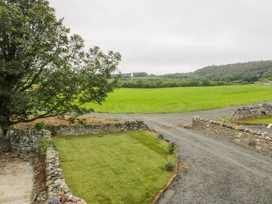 A gravel driveway with stone walls and a patch of newly laid grass with plants near a tree at Sgubor in Pentraeth