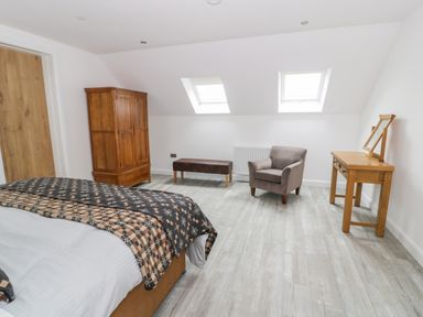 A bedroom with a bed a wooden wardrobe a bench an armchair a wooden dressing table and two skylight windows at Sgubor in Pentraeth