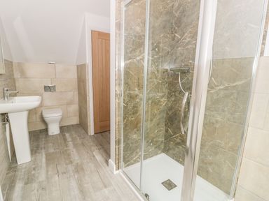 A bathroom with a glass shower enclosure a white sink and a toilet at Sgubor in Pentraeth