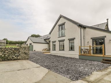 Exterior of a white house with multiple windows and a small wooden deck with chairs and table at Sgubor in Pentraeth