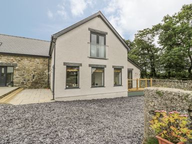 An exterior of a house with white walls stone accents and a gravel driveway at Sgubor in Pentraeth