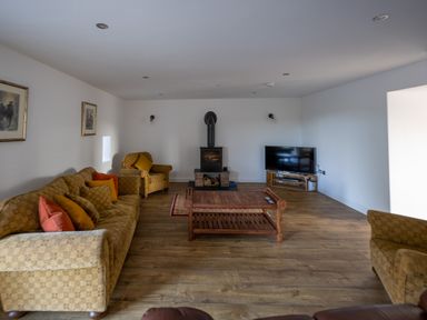 A living room with sofas and armchairs a wooden coffee table a wood stove and a television at Sgubor in Pentraeth