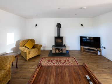 A living room with armchairs a wood stove a television and a wooden coffee table at Sgubor in Pentraeth