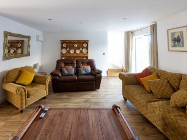 A living room with two brown sofas a wooden coffee table and a wooden shelf with decorative plates at Sgubor in Pentraeth