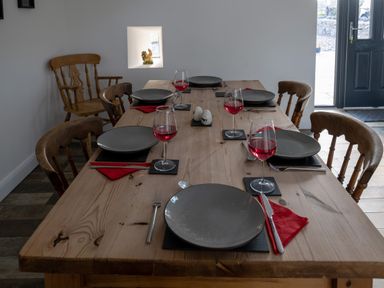 A wooden dining table with six place settings and wine glasses in a room with wooden chairs at Sgubor in Pentraeth