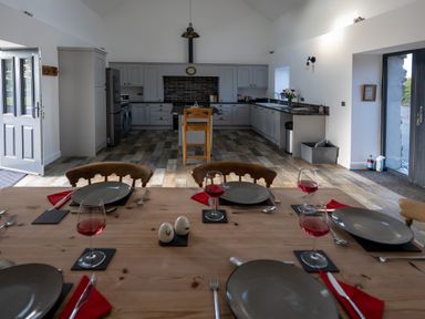 A kitchen and dining area with a wooden dining table set for four with wine glasses and plates at Sgubor in Pentraeth