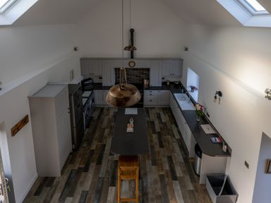 A kitchen with gray cabinets a black countertop a central island with stools and skylights at Sgubor in Pentraeth