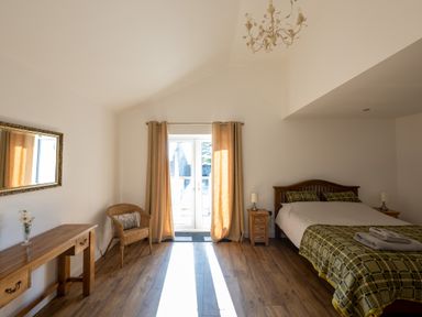 A bedroom with a bed nightstands window with curtains chair and wooden table at Sgubor in Pentraeth