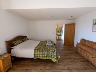 A bedroom with a bed, bedside table, wooden bench, and an open door showing a table with flowers at Sgubor in Pentraeth