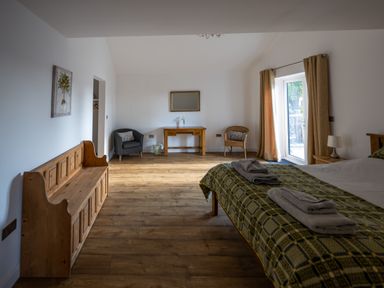 A bedroom with a bed towels wooden bench armchairs table mirror and curtains at Sgubor in Pentraeth