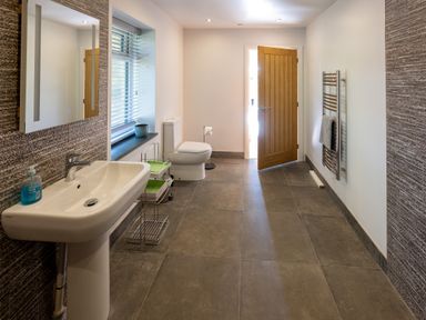 A bathroom with a sink, toilet, towel rack, window, and open wooden door at Sgubor in Pentraeth