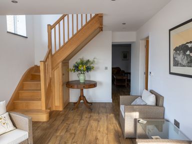 A hallway with wooden stairs a round table with a vase of flowers and wicker chairs at Sgubor in Pentraeth