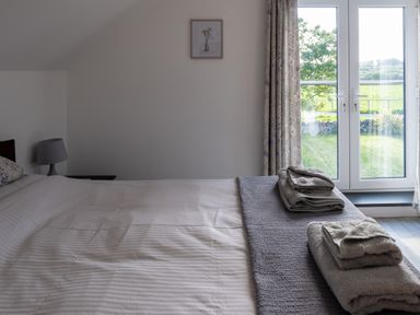 A bedroom with a bed folded towels bedside lamp and window overlooking garden at Sgubor in Pentraeth