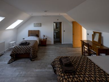 A bedroom with two single beds a wooden desk and a door leading to a bathroom at Sgubor in Pentraeth
