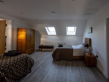 A bedroom with two beds a wooden wardrobe bench and two skylight windows at Sgubor in Pentraeth