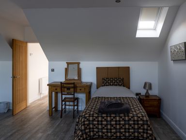 A bedroom with a single bed and a wooden desk with a mirror next to an open door at Sgubor in Pentraeth