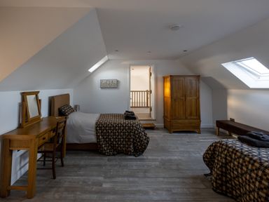 A bedroom with two single beds a wooden desk wardrobe and bench under skylights at Sgubor in Pentraeth