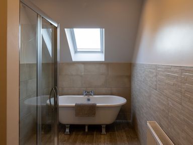 A bathroom with a bathtub under a skylight window and a glass shower enclosure at Sgubor in Pentraeth