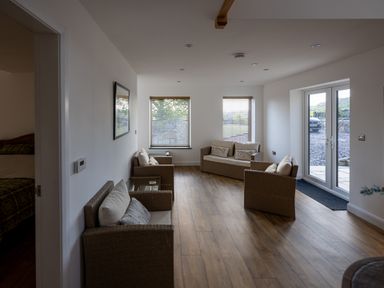 A sitting room with wicker furniture and cushions near windows and a glass door at Sgubor in Pentraeth