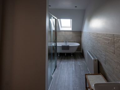 A bathroom with a freestanding bathtub under a skylight a glass shower enclosure a radiator and a small table at Sgubor in Pentraeth