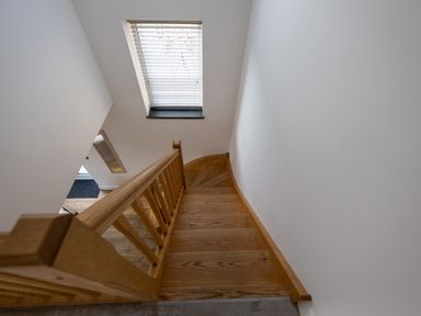 Wooden staircase with railing next to a window with blinds at Sgubor in Pentraeth