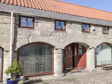 Stone building with arched windows and doors a cobblestone courtyard a blue potted plant and a bench at The Mistal in Glanton near Alnwick
