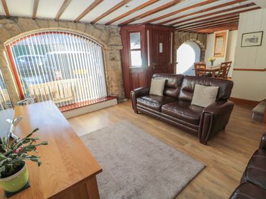 A living room with leather sofas a wooden TV stand a rug and a dining table at The Mistal in Glanton near Alnwick