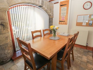 A dining area with wooden table and chairs near a stone arch window at The Mistal in Glanton near Alnwick