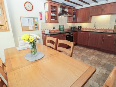A kitchen with wooden cabinets a dining table with chairs and a vase of flowers at The Mistal in Glanton near Alnwick