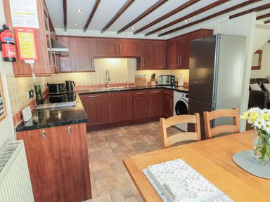 A kitchen with wooden cabinets a refrigerator a washing machine and a dining table with flowers at The Mistal in Glanton near Alnwick