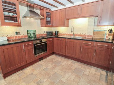 A kitchen with wooden cabinets black countertops stainless steel oven toaster kettle and a tiled floor at The Mistal in Glanton near Alnwick