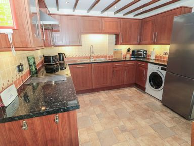 A kitchen with wooden cabinets black countertops a stainless steel refrigerator washing machine toaster kettle microwave and tiled floor at The Mistal in Glanton near Alnwick