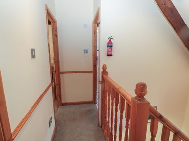A hallway with carpeted floor wooden banister and door frames with a fire extinguisher on the wall at The Mistal in Glanton near Alnwick