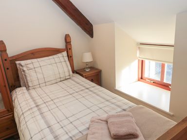 A bedroom with a wooden bed and checkered bedding a side table with a lamp and a window with a blind at The Mistal in Glanton near Alnwick