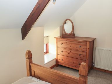 A bedroom with wooden chest of drawers with oval mirror and wooden bed frame at The Mistal in Glanton near Alnwick
