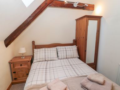 A bedroom with a double bed pillows and folded towels next to a wooden bedside table with lamp and wooden wardrobe at The Mistal in Glanton near Alnwick
