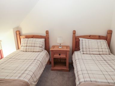 A bedroom with two single beds with checkered bedding and a wooden nightstand with a lamp between them at The Mistal in Glanton near Alnwick