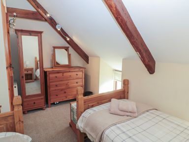 A bedroom with wooden furniture including bed wardrobe and dresser under exposed roof beams at The Mistal in Glanton near Alnwick