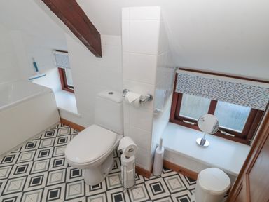 A bathroom with a toilet bathtub window and patterned floor at The Mistal in Glanton near Alnwick
